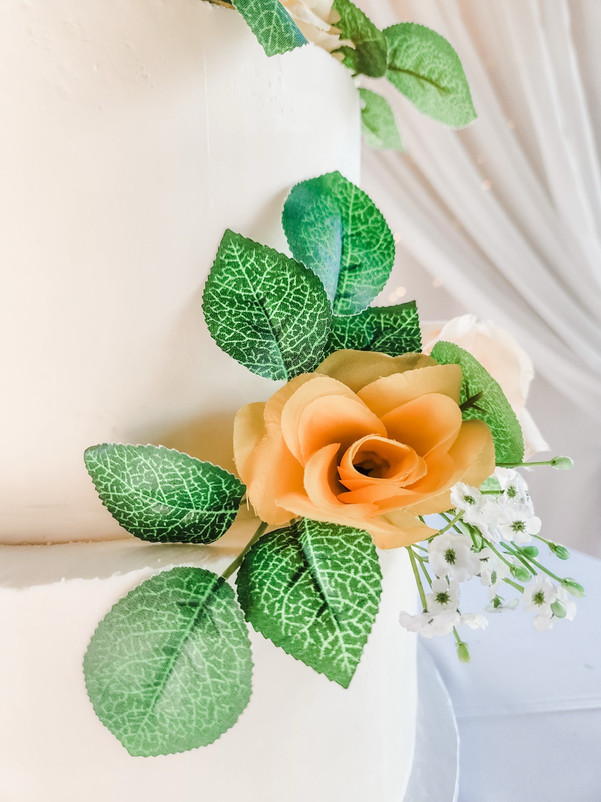 Close-up photo of peach rose and greenery on a wedding cake